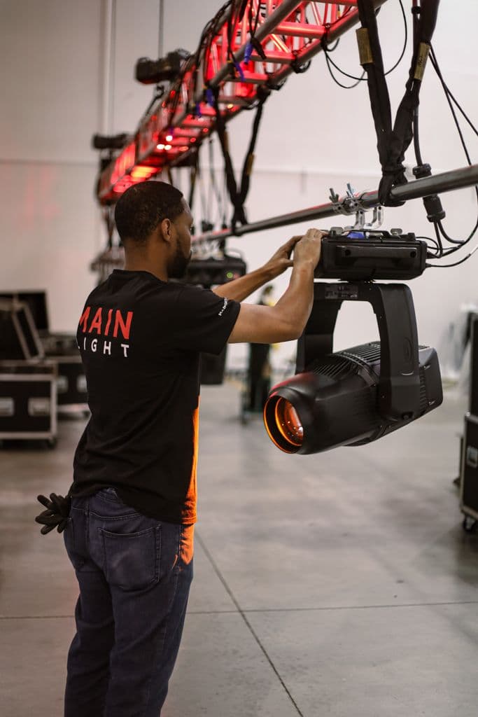 Elation Proteus Hybrid being adjusted by a Main Light employee while hanging on truss.